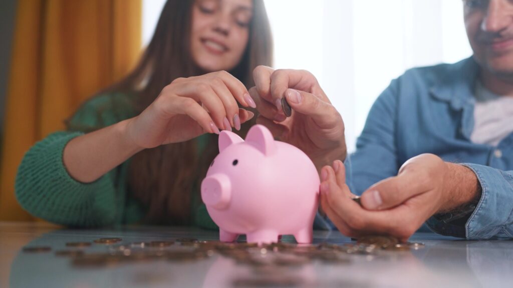 Educação financeira adolescentes: jovem coloca moedas em um cofre ao lado de um homem 